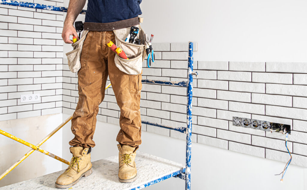 Electrician construction worker in work clothes on a stepladder.